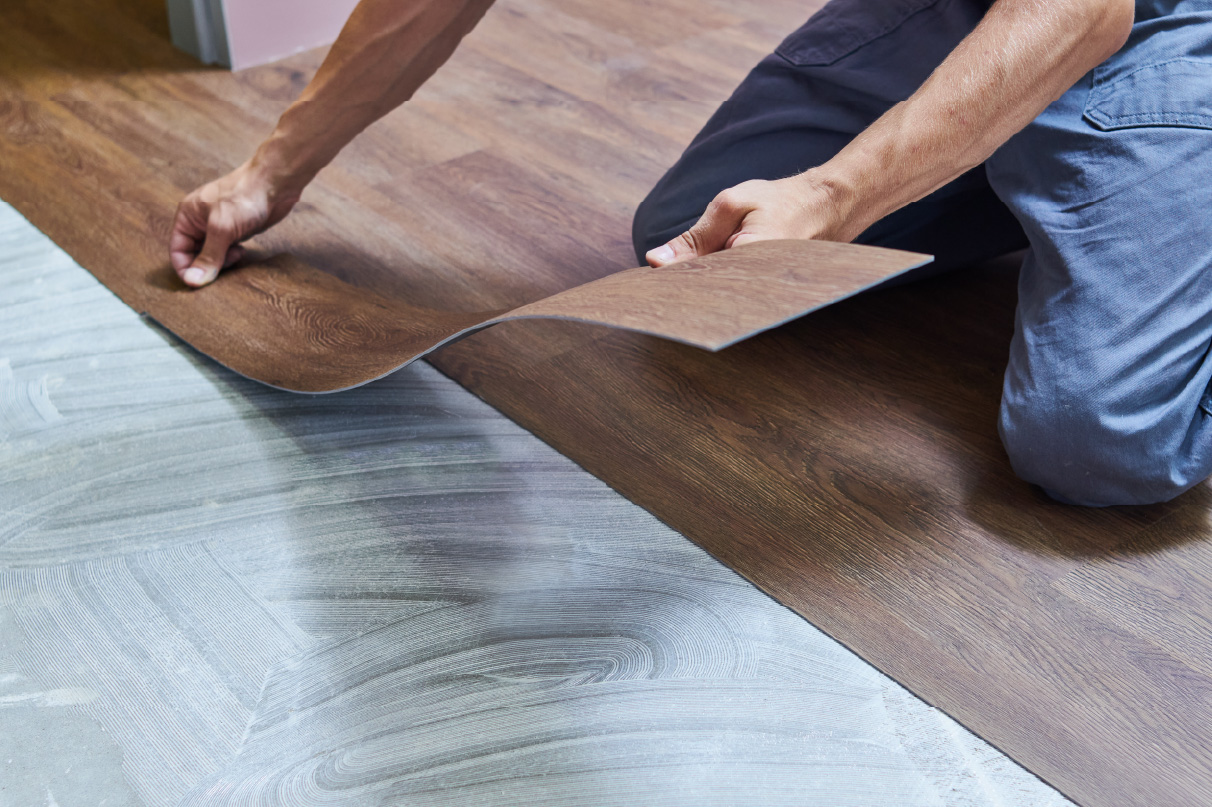 Person laying vinyl plank flooring over adhesive on a smooth subfloor.