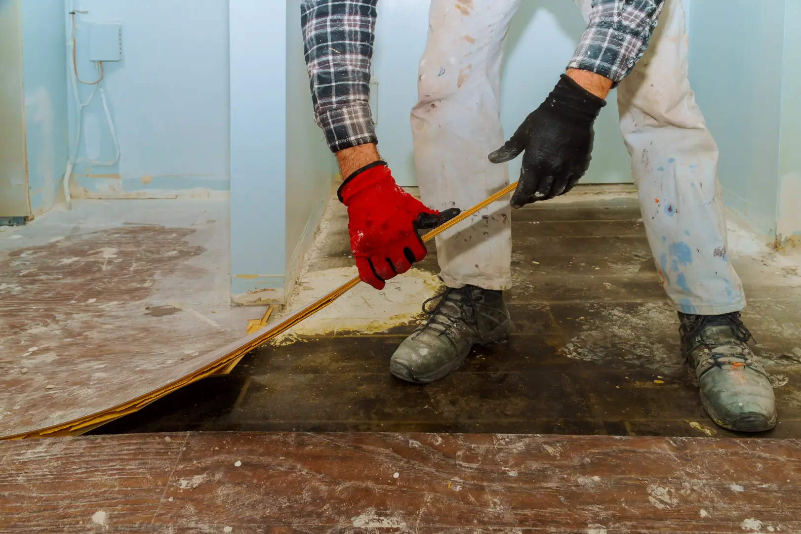 Worker removing damaged flooring panels from a room during a renovation project.
