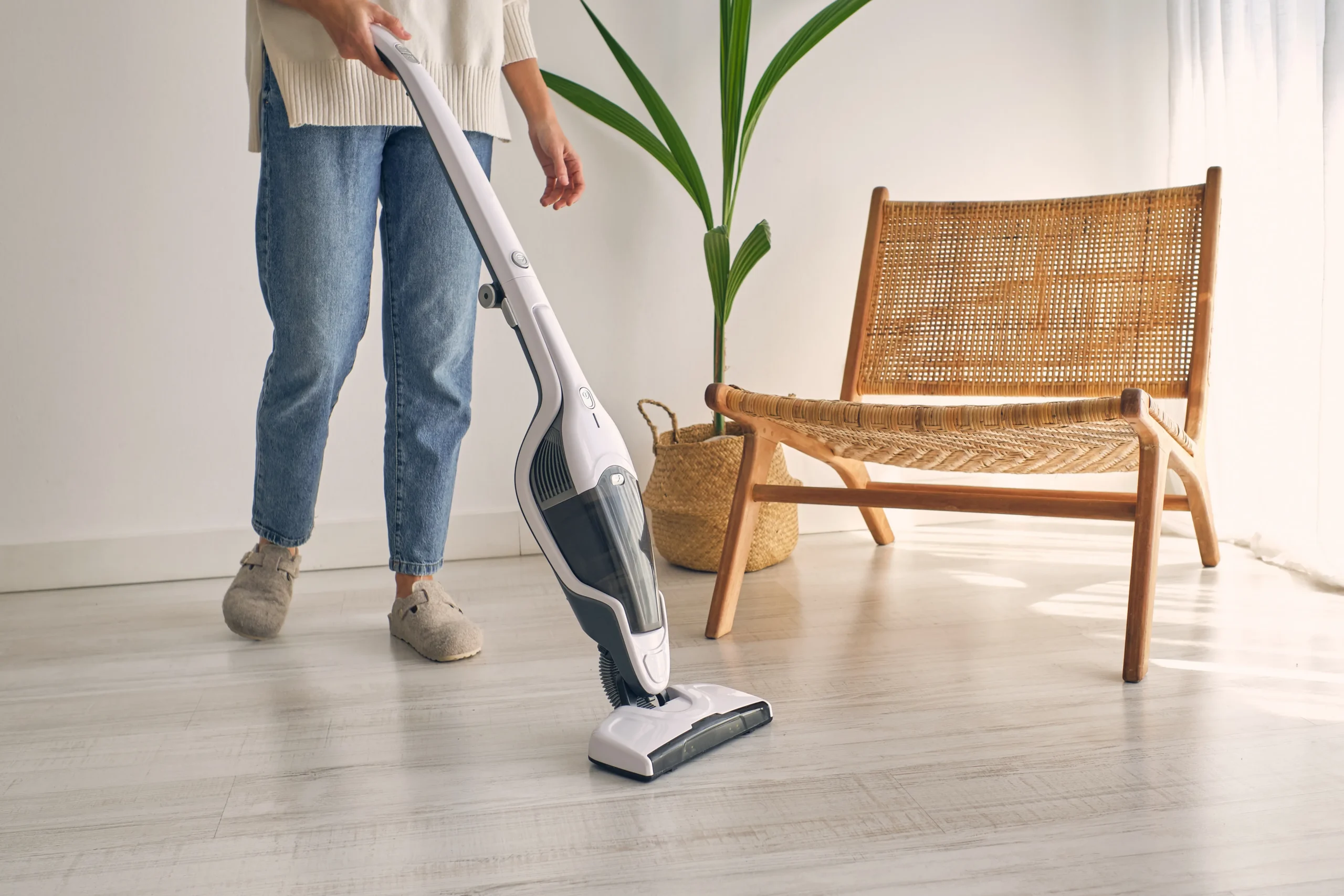 Person vacuuming a hard surface floor in a bright living room with modern furniture.