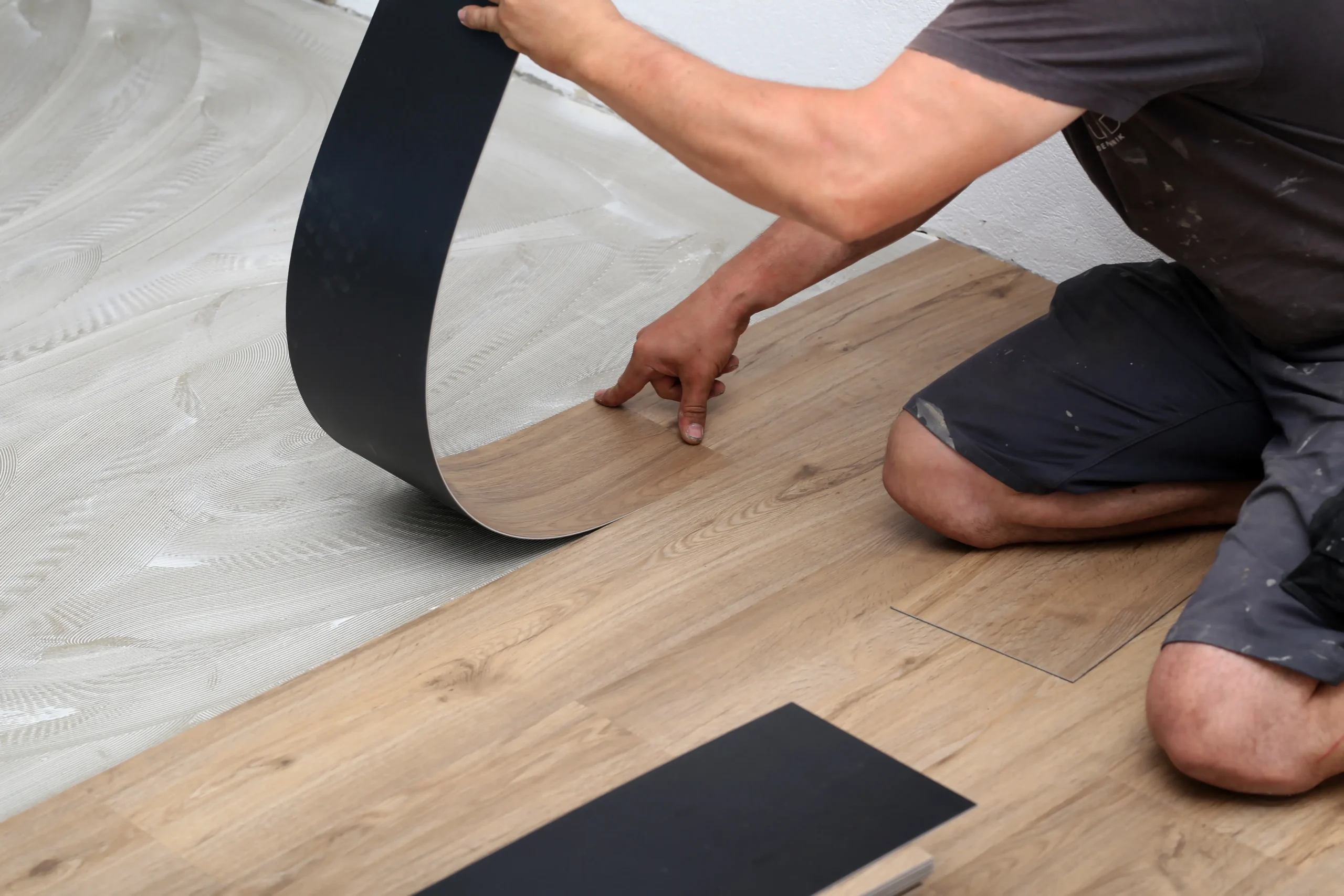 Installer placing a vinyl flooring sheet onto an adhesive-coated subfloor during installation.