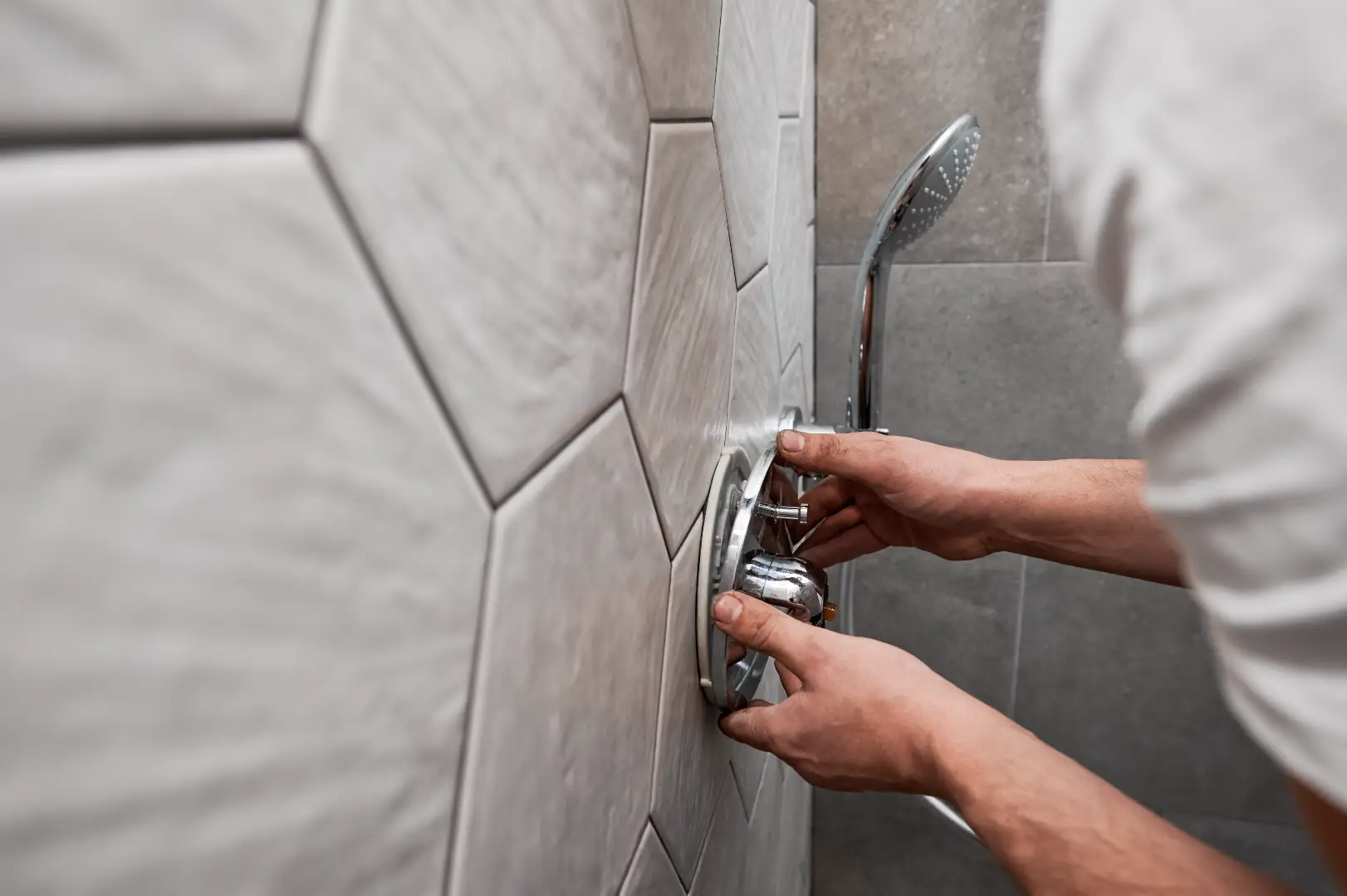 Person installing a shower control handle on a tiled walk-in shower wall.