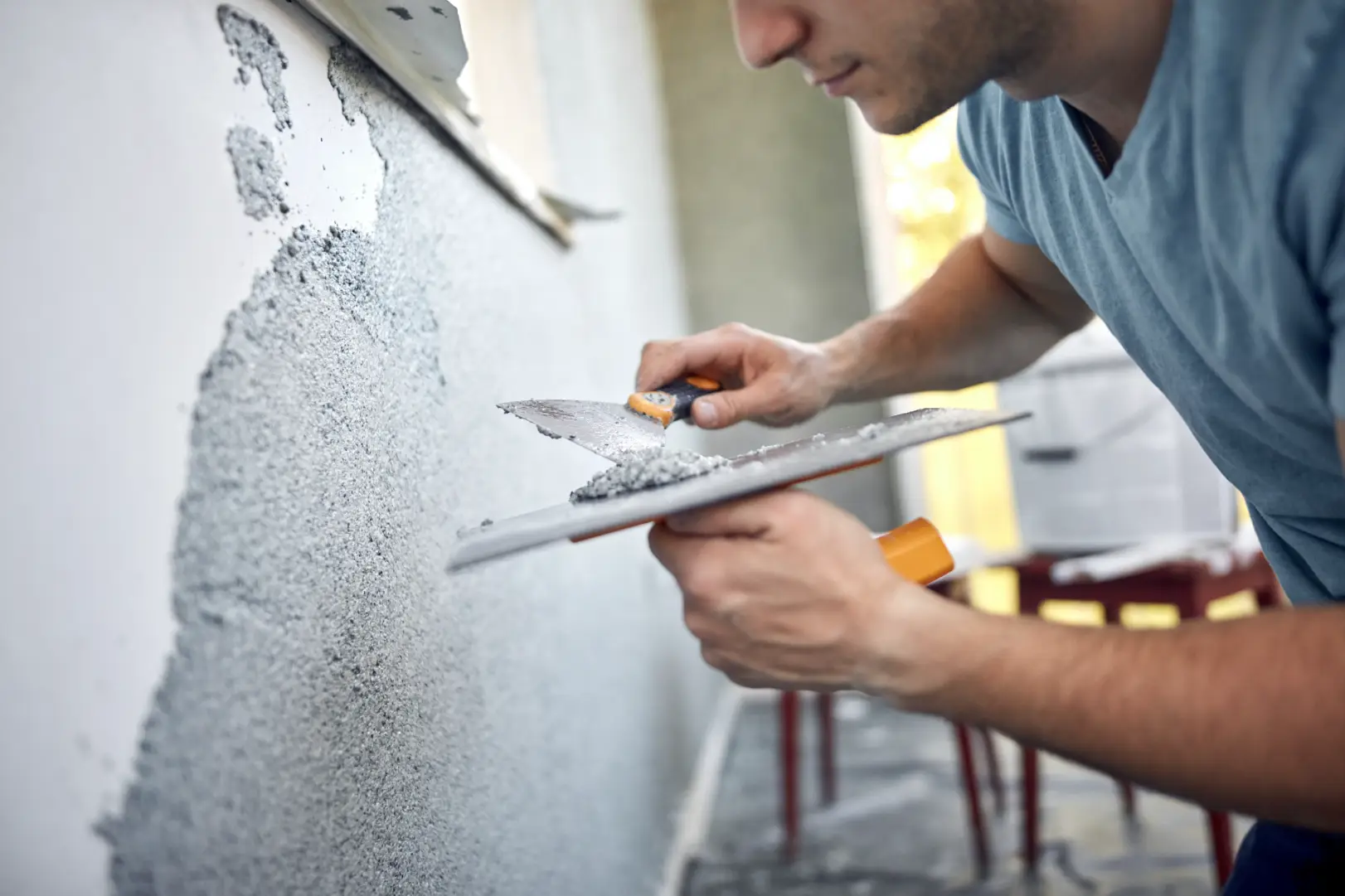 Contractor applying plaster to a damaged wall using a trowel and hawk.