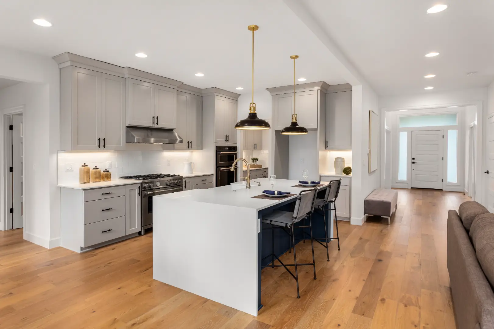 Modern kitchen with white cabinetry, large island, pendant lights, wood flooring, and bar stools.
