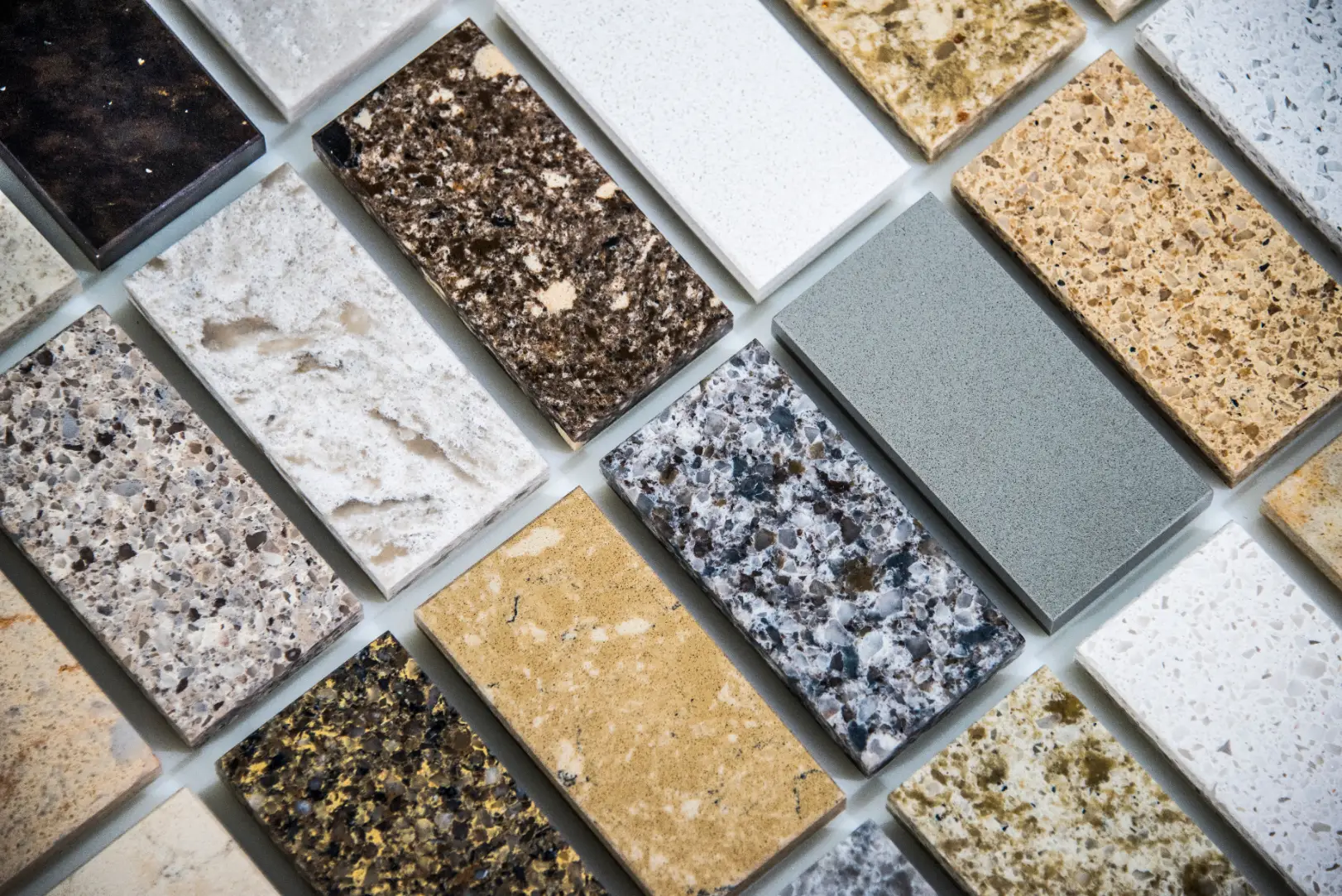 Rectangular stone and engineered surface samples in varied colors and patterns arranged on a table.